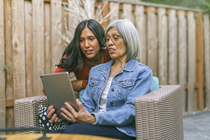 Older adult woman sitting outside while showing tablet to older adult daughter.
