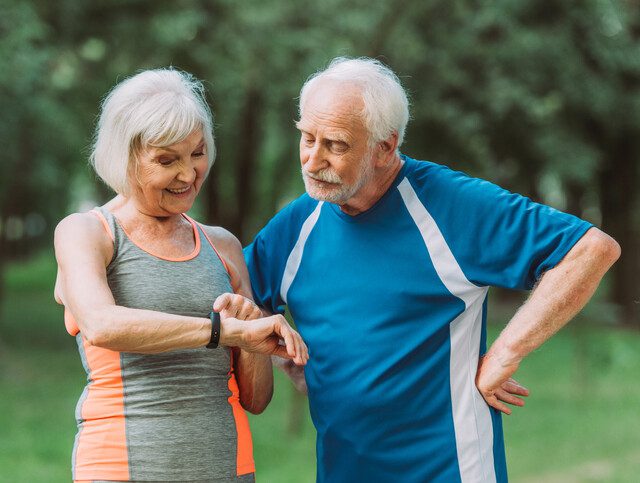 Smiling senior woman looking at fitness tracker near husband in park