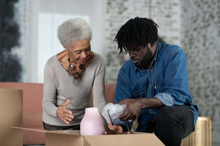 A young man of African descent and his mother have just moved into a new house and are unpacking a box together.